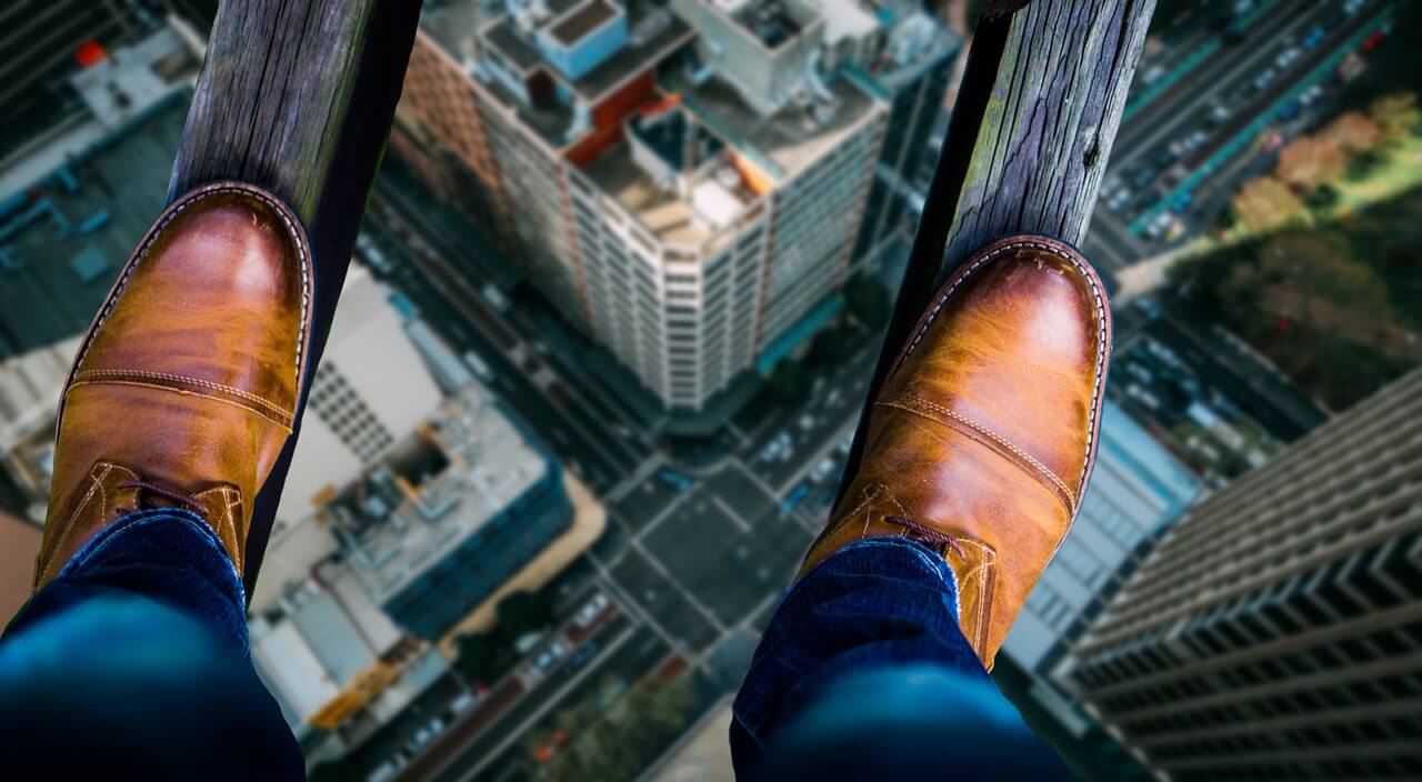 Photo d'une personne marchant sur 2 planches dans le vide au dessus d'une ville américaine. Il semble avoir peur ou en avoir la phobie.