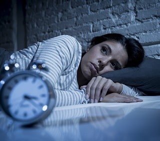 Photo d'une personne cherchant le sommeil en regardant son réveil